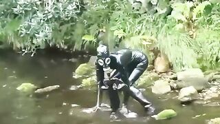 Outdoor walk in the wood and river washroom full encased in ebony latex catsuit and rubber gas mask